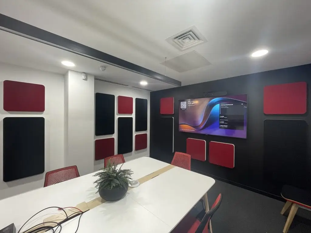 Q-PARKs main Board Room with red and black acoustic panels, mounted display screen showing a desktop background, and white conference table with chairs.